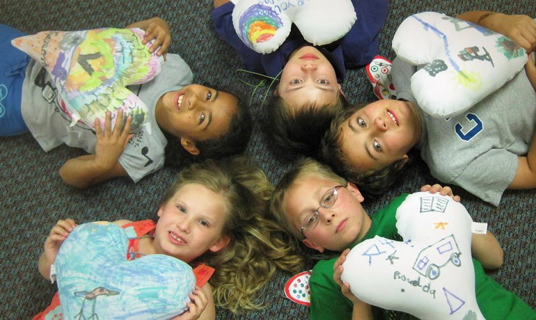 New Song children lying in a circle holding decorated heart ballons