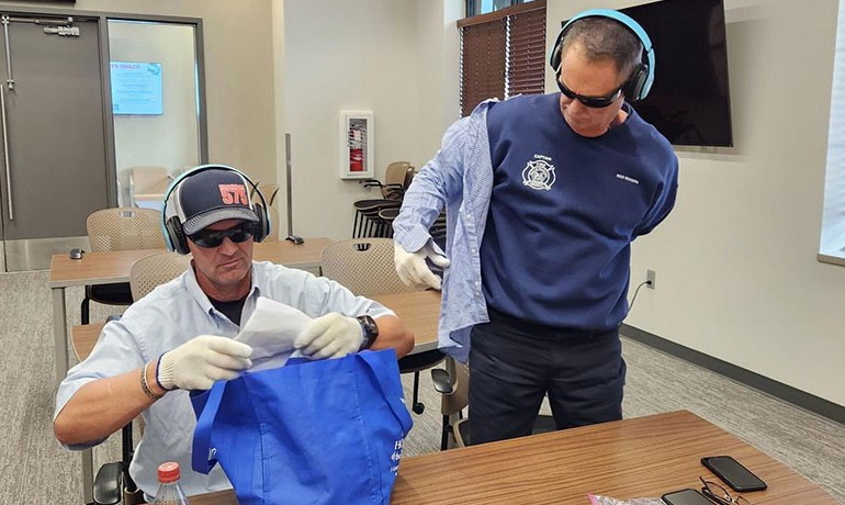 As part of a training exercise to help them understand the challenges facing those suffering from dementia, Jared Hobson and Reid Rodgers of the Maricopa Fire/Medical Department try to perform routine tasks while wearing static-emitting headphones and thick gloves.